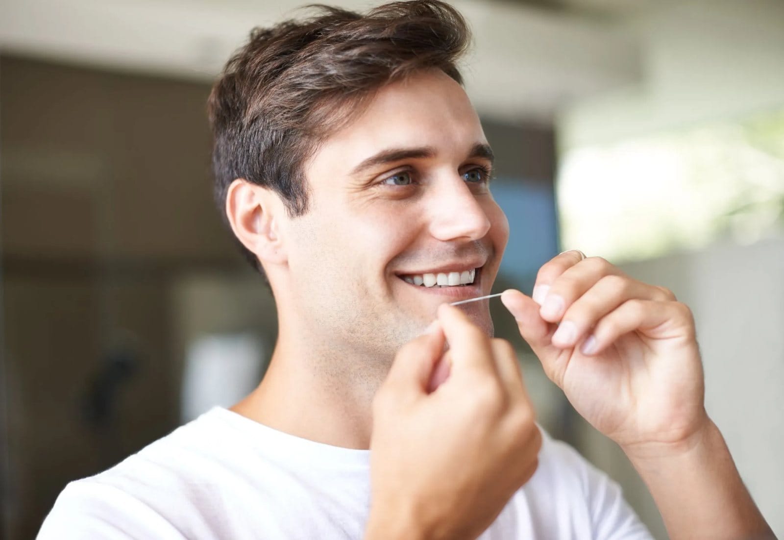 A smiling young man flossing his teeth
