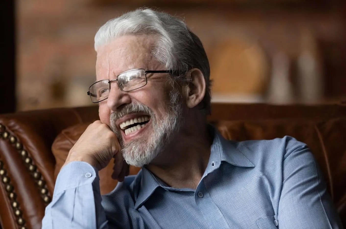 A laughing older man with a grey beard and glasses