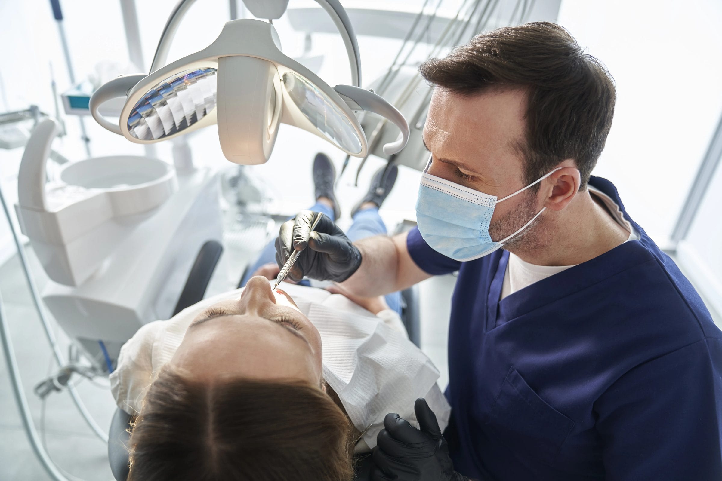 A dentist examining a patient’s teeth in a bright treatment room