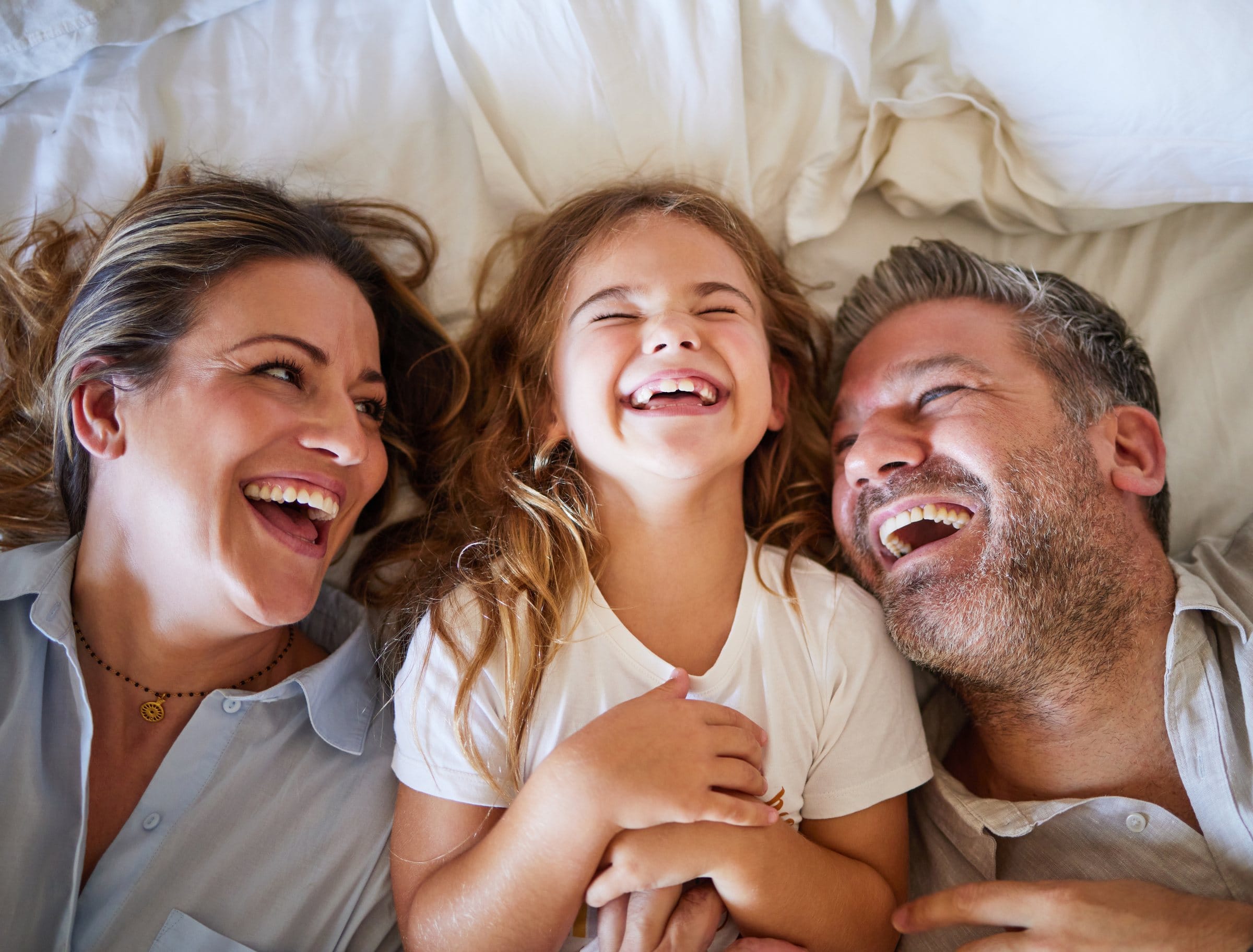 A mother, father and young daughter lying side by side, laughing together