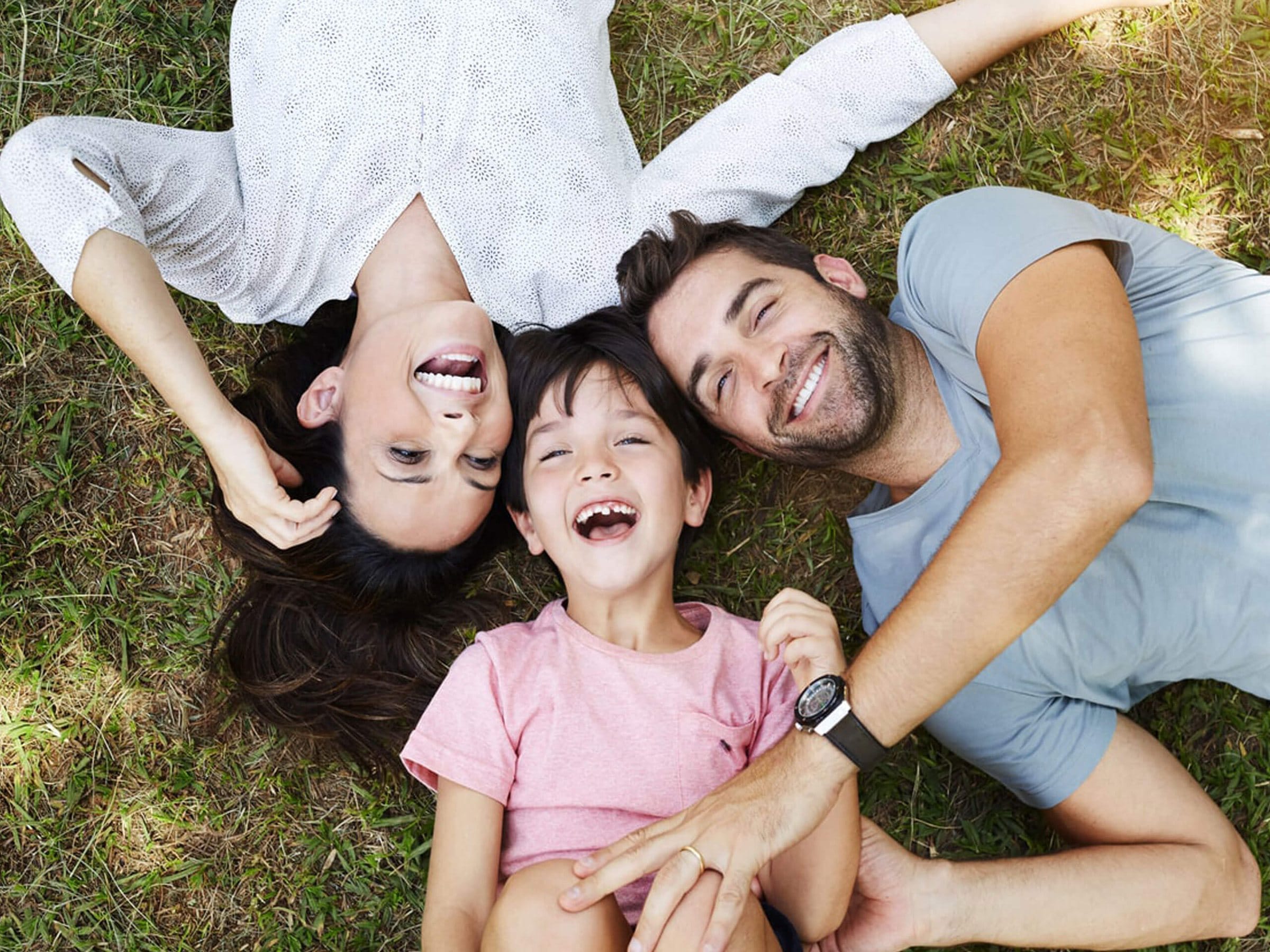 A mother, father and daughter lying on the grass, laughing together