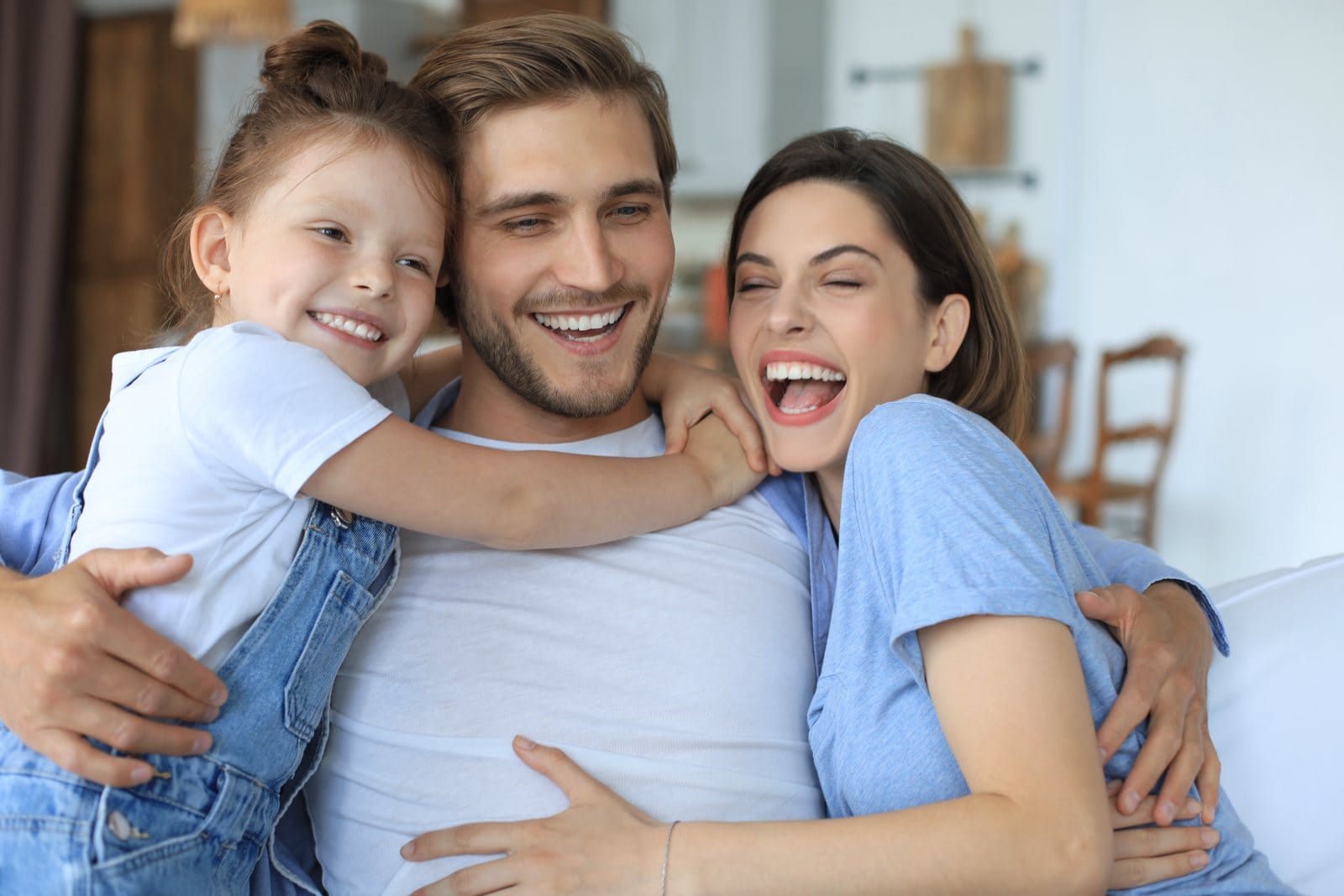 Two parents and their young daughter smiling together on a sofa
