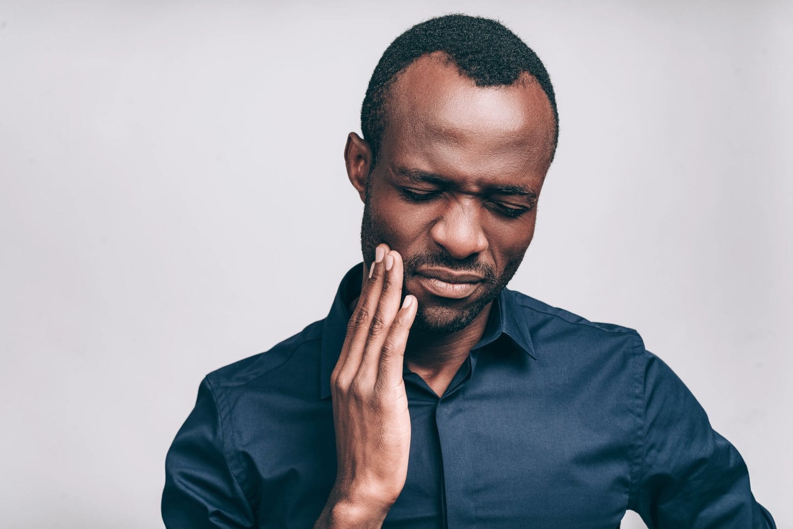 A man holding his cheek with his eyes closed in pain