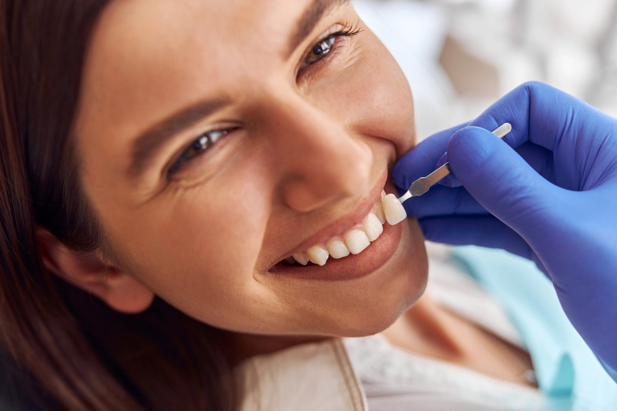 A dental professional holding a shade sample beside a smiling patient’s teeth