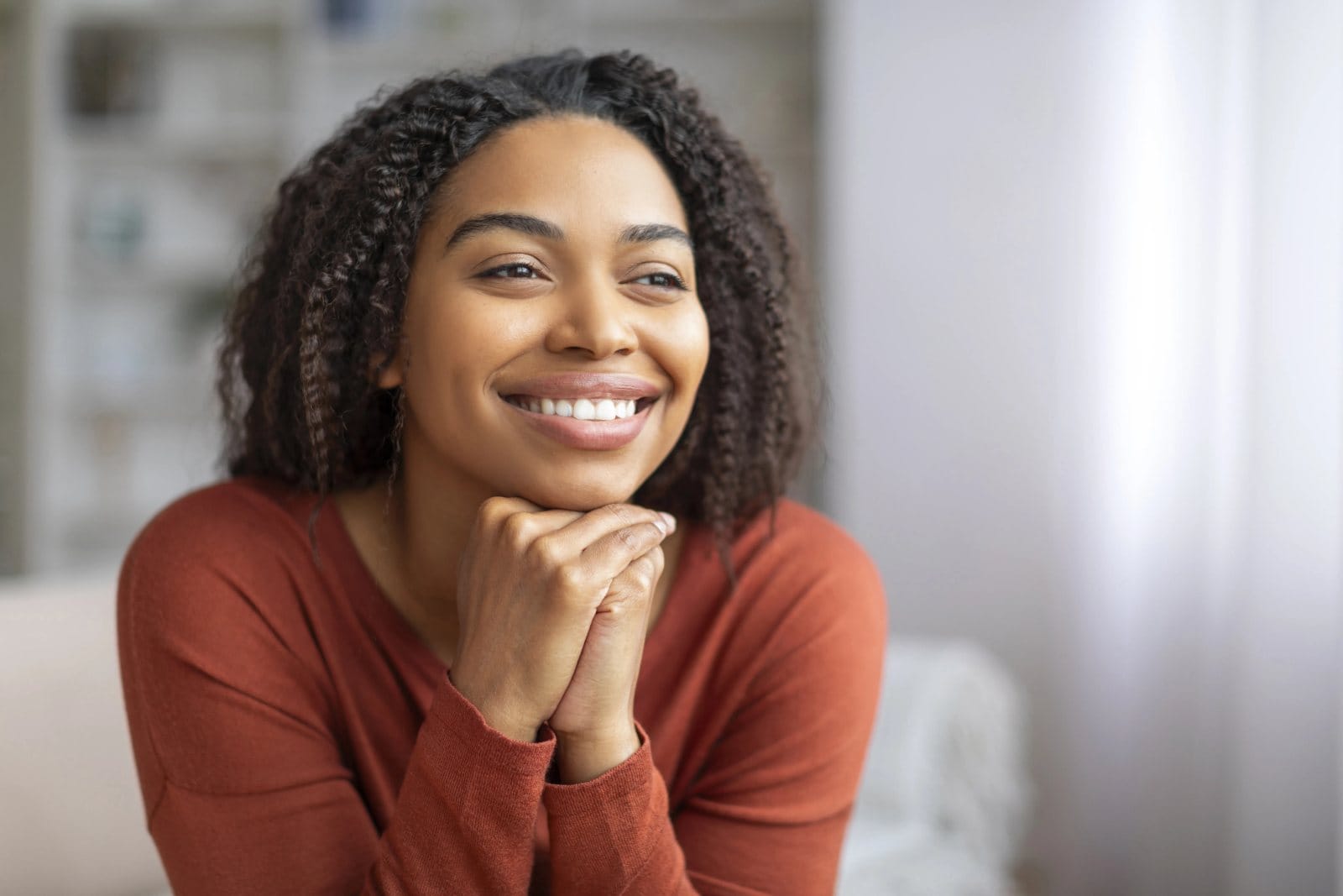 A smiling young woman resting her chin on her hands at home