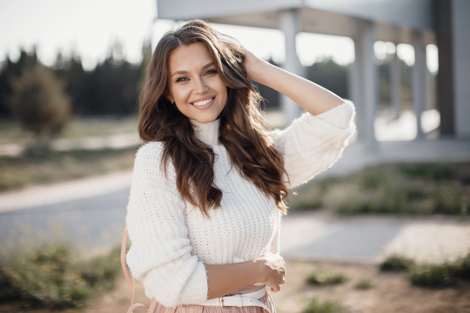 A smiling young woman in a white sweater outdoors