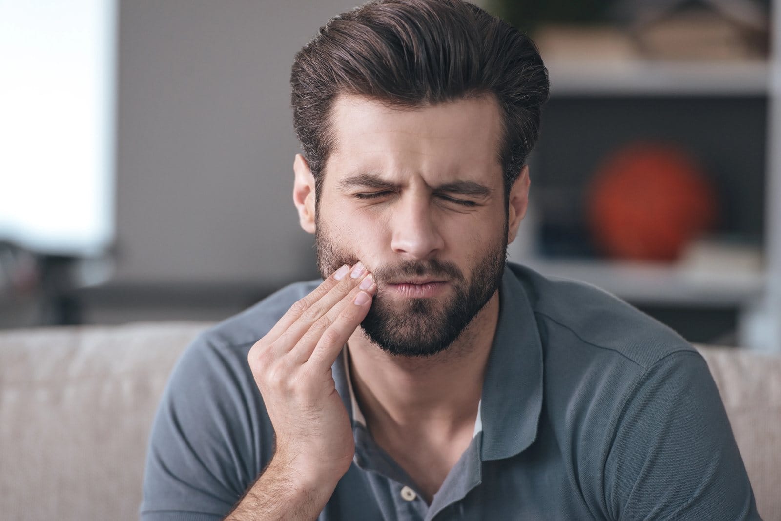 A man on a sofa holding his jaw in pain